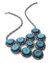 Go for glitter and perfect your party look. This festive bib necklace boasts rows of blue plastic cabochon stones with a glittery finish. Crafted in hematite tone mixed metal. Approximate length: 18 inches + 2-inch extender. Approximate drop: 3 inches.